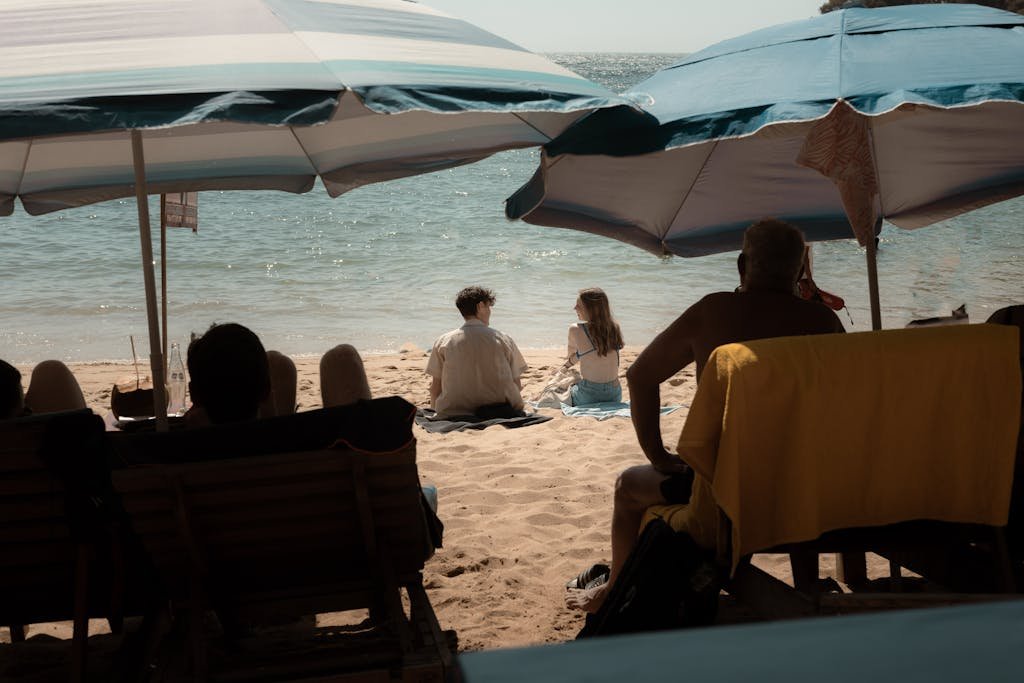 A couple enjoying a sunny beach day under umbrellas with a scenic ocean view.