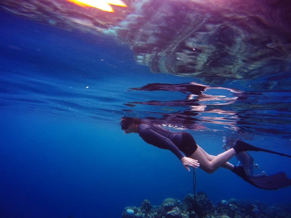 A freediver gracefully swims above a colorful coral reef, immersed in the clear blue ocean.